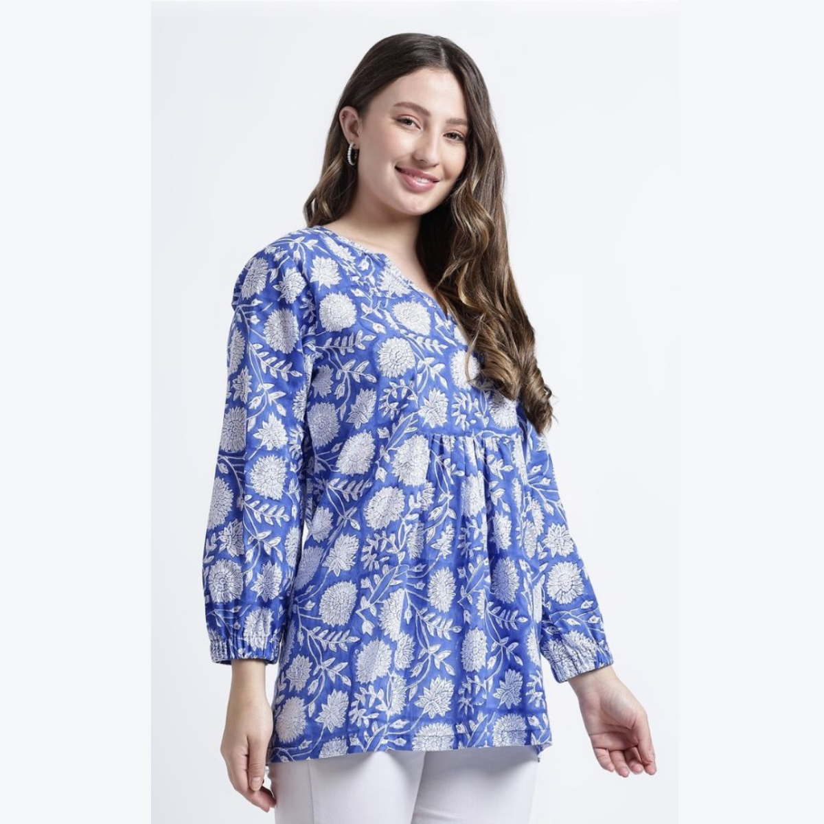 Blue Printed Tunic: A smiling model wearing a bright blue tunic with white floral patterns. The garment features long sleeves and a loose, flowy fit, showcasing traditional textile craftsmanship.